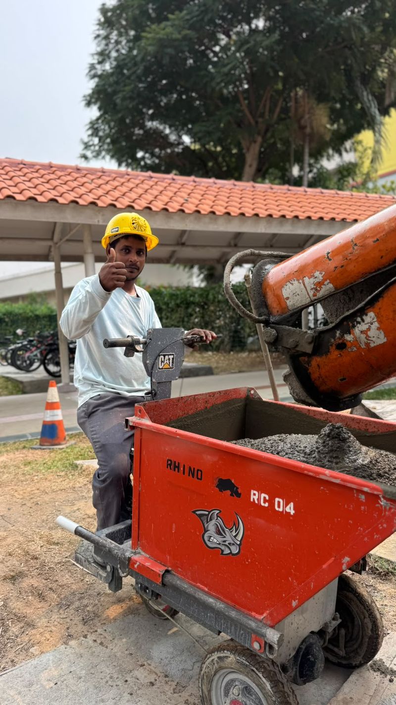 Team member in a yellow hard hat giving a thumbs up beside an orange Rhino Crete-branded dumper while concrete is loaded from a mixer chute.
