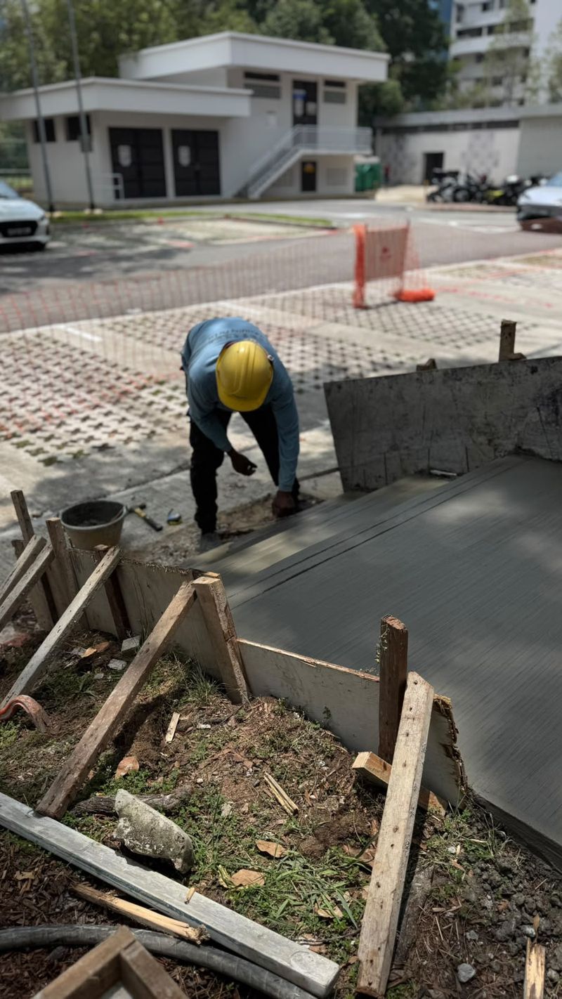 Freshly placed concrete surface enclosed by timber edge formwork, with a worker bending at the edge in the background.